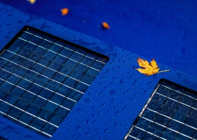 Gros plan sur un panneau solaire bleu avec des gouttes d'eau et une feuille jaune posée dessus.