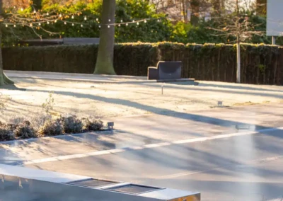 Une terrasse avec une piscine couverte par une structure métallique, entourée d'arbres et de buissons, sous un ciel clair.