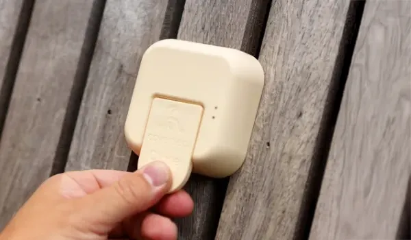 modeles-automatique-2 Une main tient un dispositif beige fixé sur une surface en bois, avec des panneaux en arrière-plan.