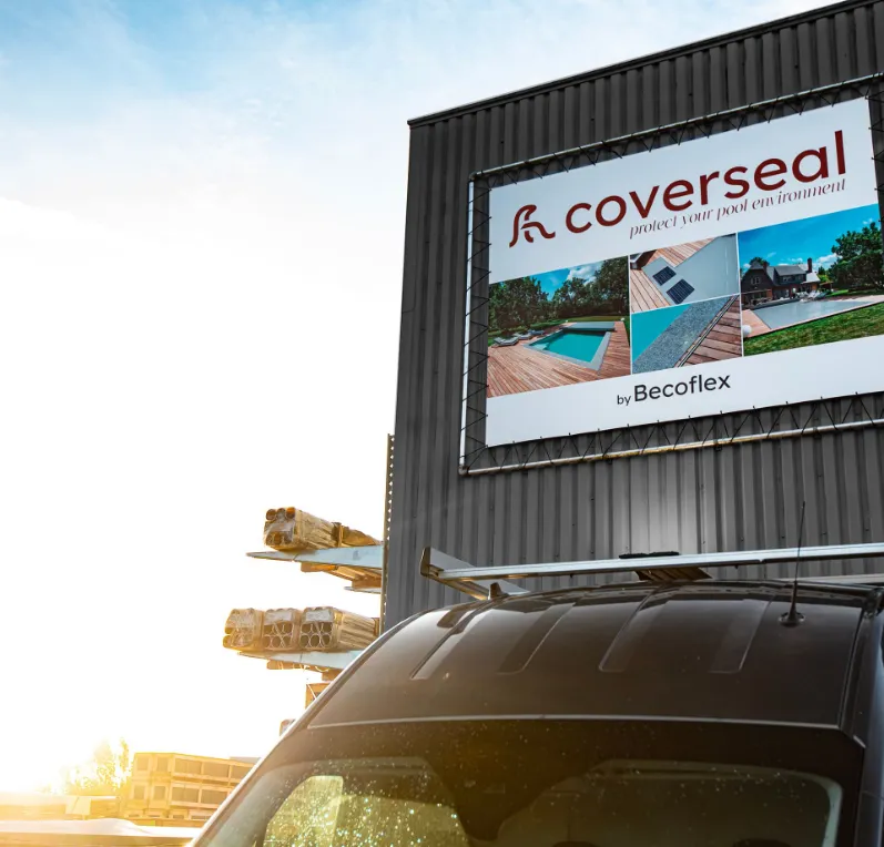 notre-entreprise Panneau publicitaire "Coverseal" sur un bâtiment gris, avec des images de piscines et une voiture au premier plan.