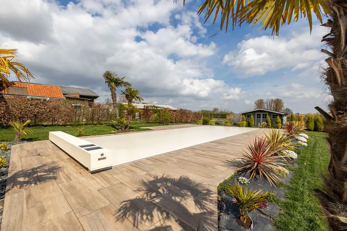 Une piscine couverte par un abri blanc est entourée de palmiers et de plantes colorées, avec un cabanon en arrière-plan.