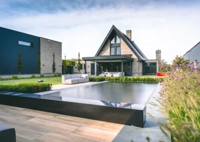 Maison moderne en briques avec toit en pente, entourée d'un jardin vert, piscine couverte et mobilier de jardin gris.