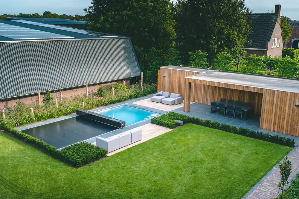 veerle-et-jan-coverseal Piscine extérieure couverte à côté d'un salon de jardin en bois avec des canapés gris, entourée de pelouse et de haies.