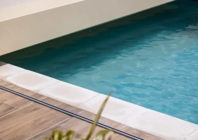 Une piscine avec de l'eau turquoise, bordée de dalles blanches et de carrelage effet bois.
