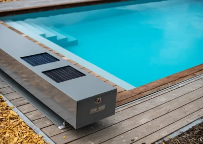 Dispositif en métal gris avec panneaux solaires à côté d'une piscine bleue, entourée de margelles en bois et de copeaux de bois.
