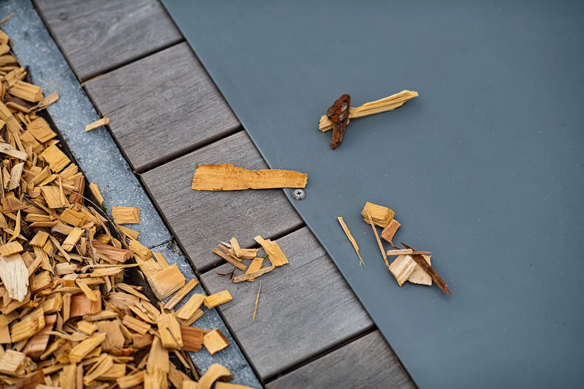 comment-faire-pour-mettre-sa-piscine-en-hivernage Des copeaux de bois dispersés sur une terrasse en bois gris et une couverture de piscine grise.