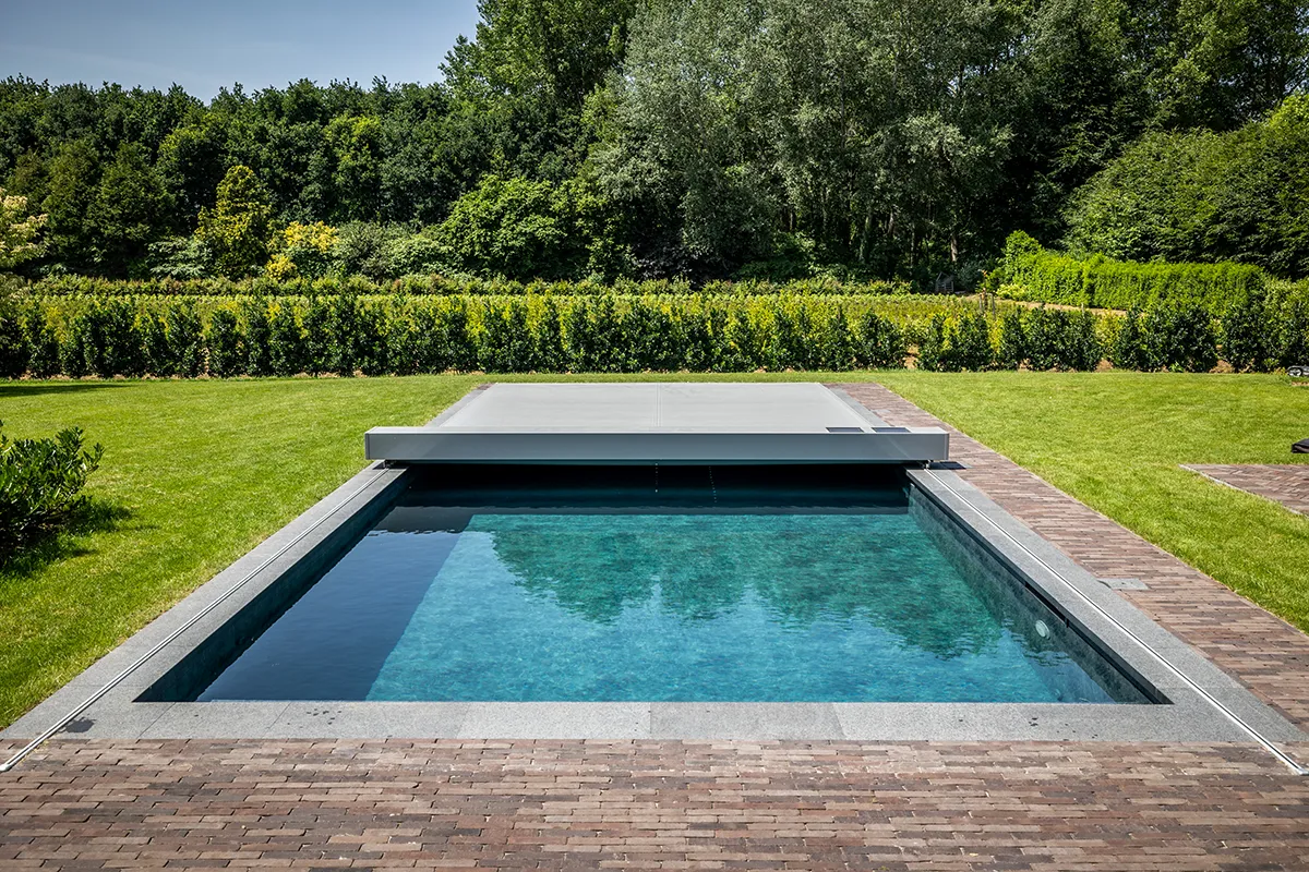 Piscine rectangulaire avec couverture grise Coverseal, entourée de pelouse verte et d'une haie, sous un ciel bleu clair.
