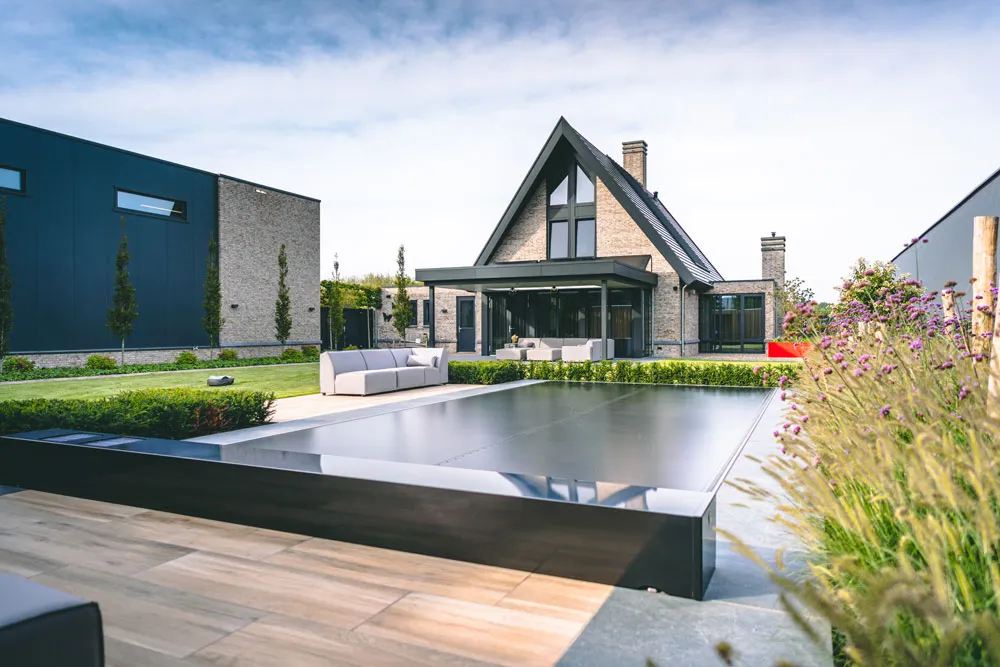 Maison moderne avec toit en pente, entourée de jardin verdoyant, terrasse en bois et piscine couverte avec une Coverseal.