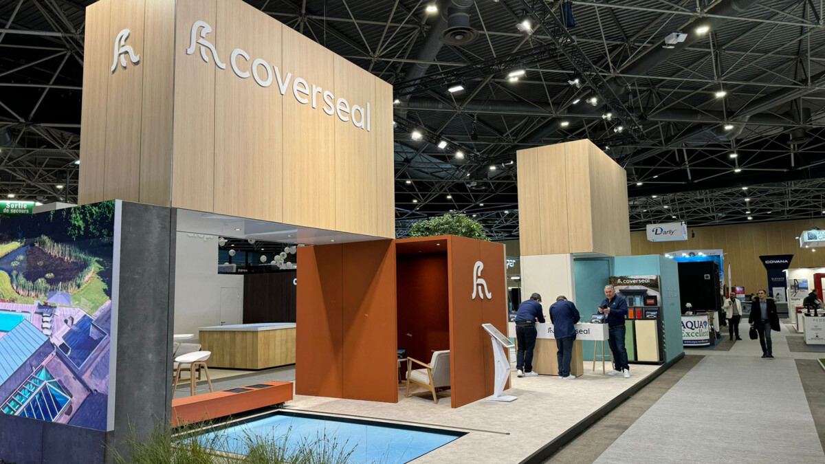 Stand d'exposition avec le logo Coverseal, un écran montrant une piscine, et plusieurs personnes discutant devant.
