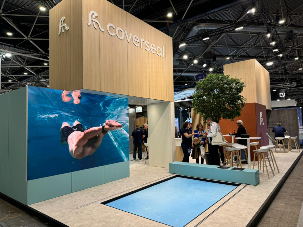 Stand d'exposition avec le logo Coverseal, un écran montrant une piscine, et plusieurs personnes discutant devant.