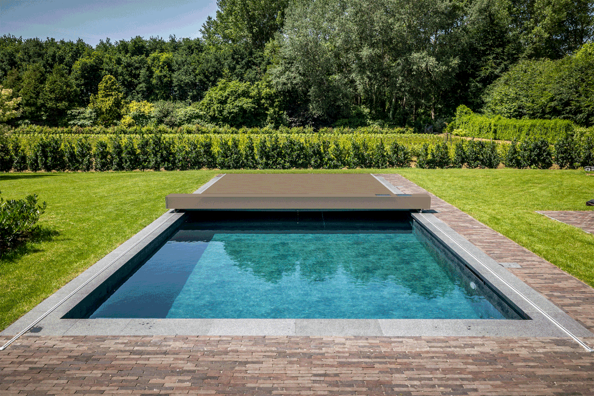PEPINIERE_GIF_Little Quatre chaises longues grises sont disposées sur une terrasse en bois autour d'une piscine rectangulaire dans un jardin verdoyant.