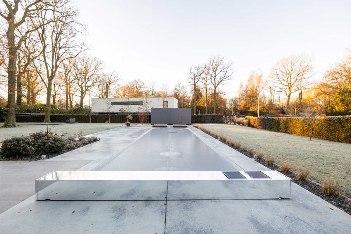 Coverseal Automatique Effet Miroir Une piscine couverte d'un volet miroir est entourée d'un jardin avec des arbres dénudés et une pelouse givrée.