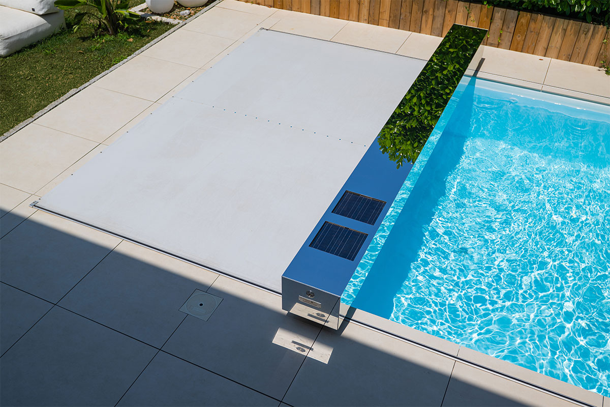 Coverseal-landscape Piscine moderne recouverte d’une couverture Coverseal beige, avec habillage effet miroir équipé de panneaux solaires, intégrée dans une terrasse carrelée.
