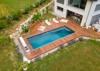Piscine rectangulaire contemporaine entourée d’une terrasse en bois avec transats et salon extérieur.