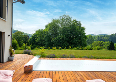Piscine recouverte de la Coverseal Automatique sur terrasse en bois, avec vue panoramique sur un grand jardin arboré.