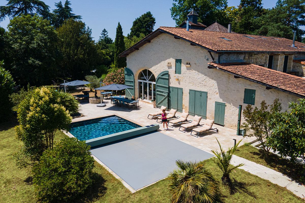 Vue aérienne d’une maison en pierre avec piscine équipée d’une couverture Coverseal grise, intégrée harmonieusement dans la terrasse en pierre claire.