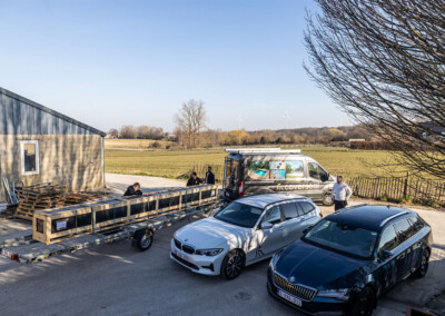 Une camionnette Coverseal et plusieurs voitures stationnées devant un entrepôt, avec des techniciens manipulant une structure longue sur une remorque.