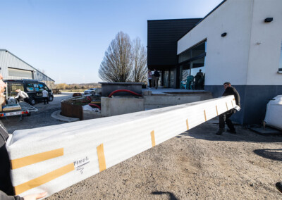 Deux techniciens transportent l'habillage de la Coverseal emballée en mousse blanche devant une maison moderne en construction.