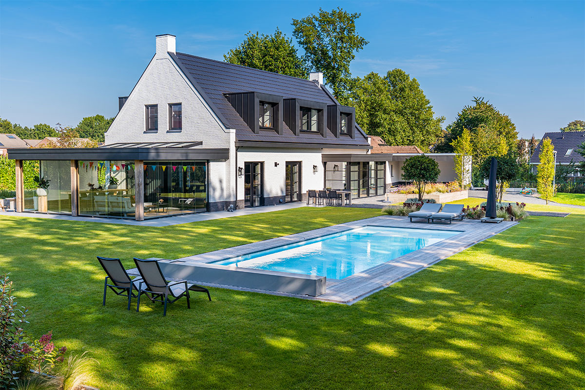 Maison moderne avec grande baie vitrée et piscine rectangulaire équipée d’une couverture Coverseal, entourée d’un jardin paysager verdoyant.