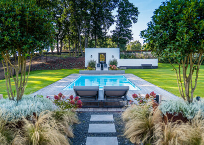 Vue d’ensemble de la piscine et du jardin, avec la couverture Coverseal et un espace détente sur une terrasse en bois entourée de végétation.