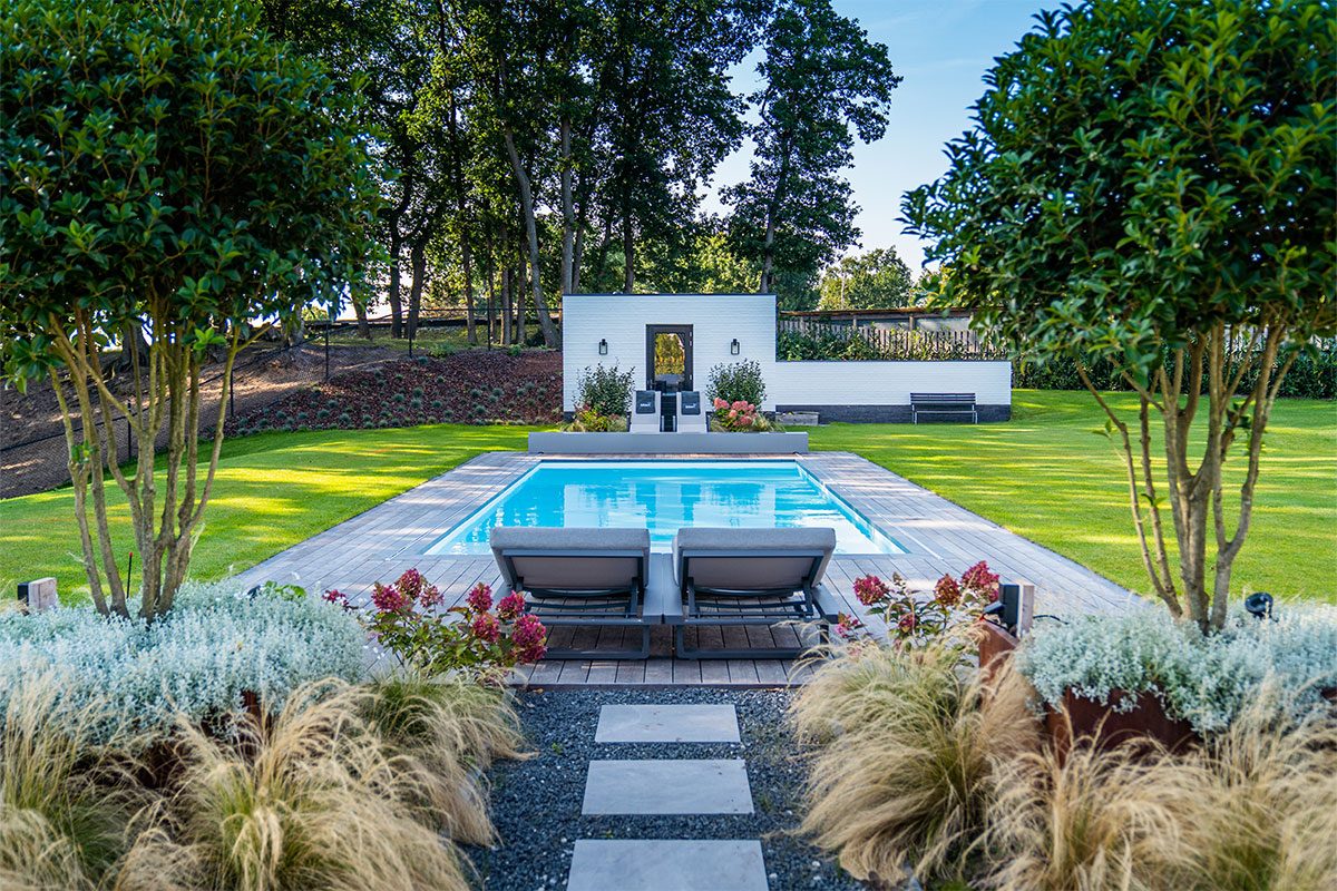 Marleen-&-Geert1 Vue d’ensemble de la piscine et du jardin, avec la couverture Coverseal et un espace détente sur une terrasse en bois entourée de végétation.