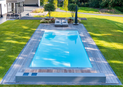 Piscine rectangulaire équipée d’une couverture Coverseal, intégrée dans une terrasse en bois au cœur d’un grand jardin.