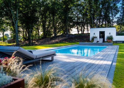 Terrasse en bois avec piscine équipée d’une Coverseal, transats gris et espace paysager avec arbres et massifs fleuris.