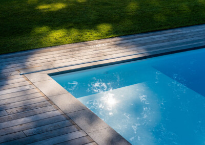 Détail du rail de la couverture Coverseal parfaitement intégré dans la terrasse en bois autour de la piscine.