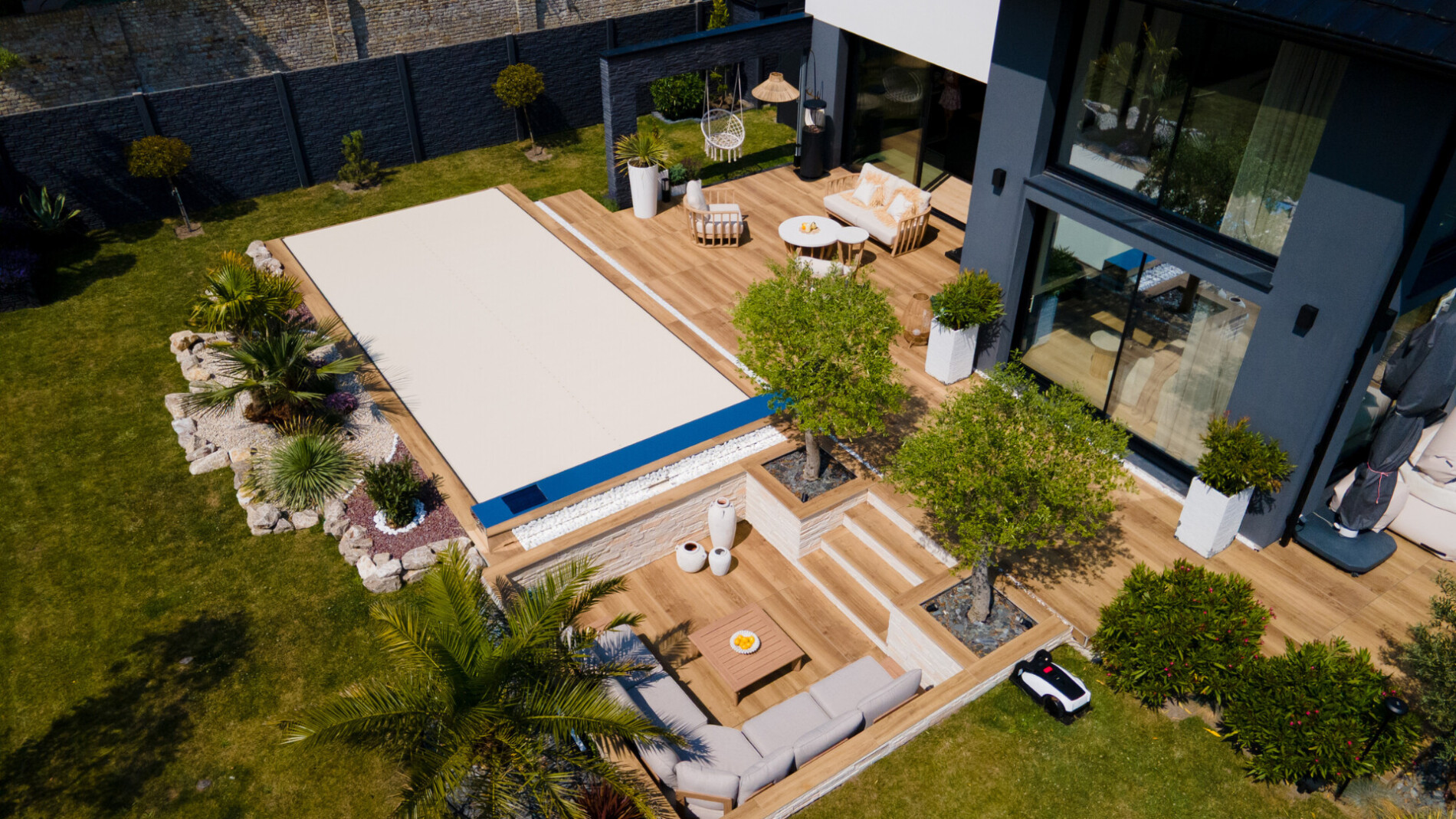 Une couverture de piscine avec un effet miroir et des panneaux solaires, entourée d'une pelouse verte et d'un carrelage beige.