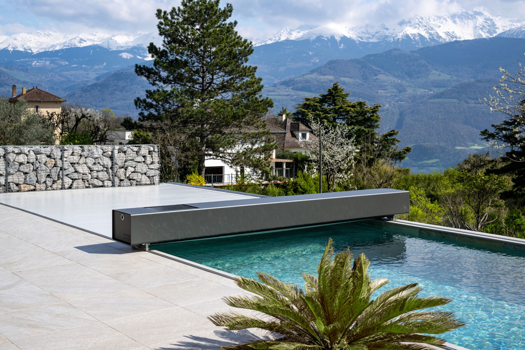 Une maison moderne en bois sombre avec de grandes fenêtres en verre, entourée de verdure et d'une pelouse verte.